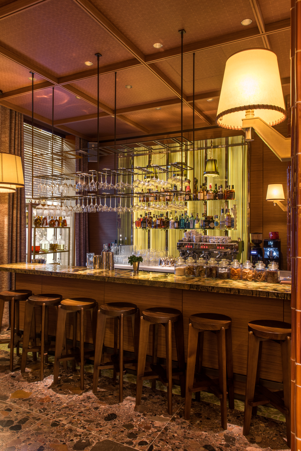 Bar à cocktails du Brach Madrid avec éclairage tamisé, tabourets en bois et verrerie suspendue.